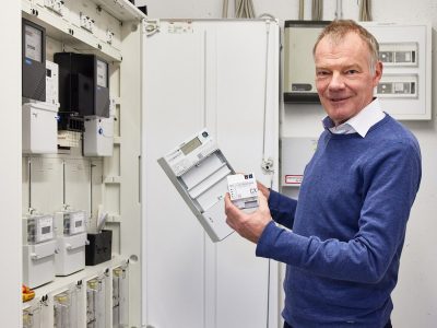 Smart Metering: Gero Lücking hält das Herzstück einer nachhaltigen, digital gesteuerten Stromversorgung in der Hand: Ein intelligentes Messsystem, das aus einem digitalen Stromzähler und einem Smart-Meter-Gateway besteht.